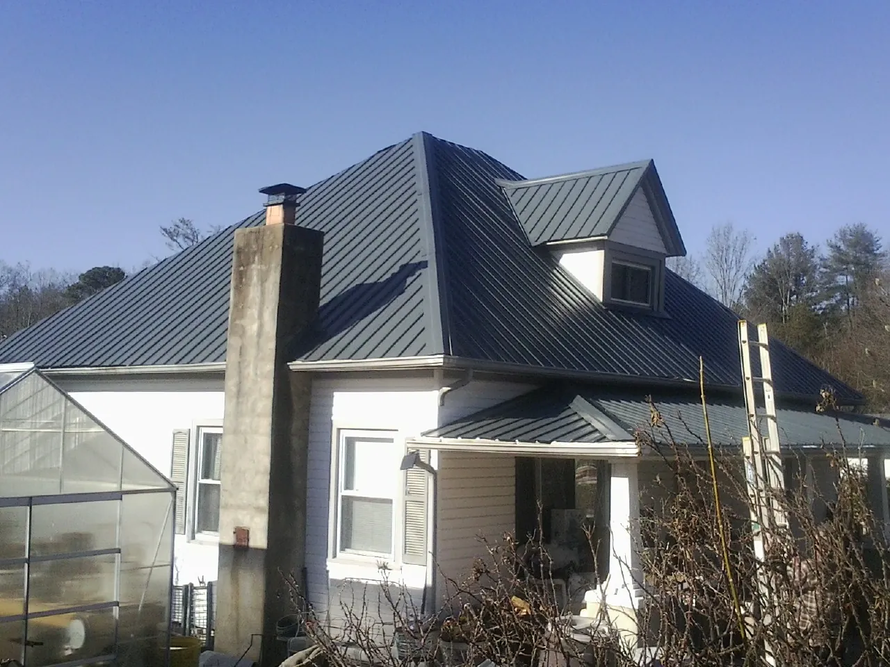 Dark blue standing seam metal roof on a white farmhouse with dormer — Slate & Tile Roof Repair by Roofing Brothers in Swanville