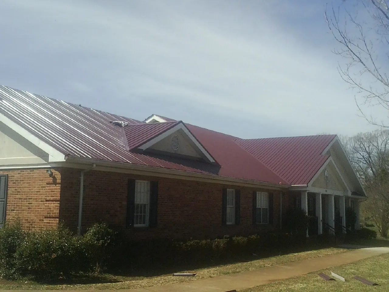 Red metal roof with gabled entries on a long brick building, from a Hail Damage Roof Repair job in Swanville