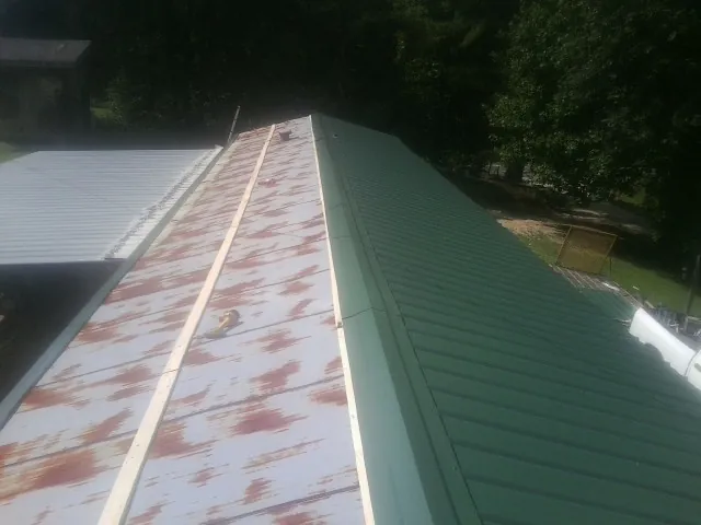 Old rusted panels beside newly installed green metal roofing — Wind Damage Roof Repair by Roofing Brothers in Swanville