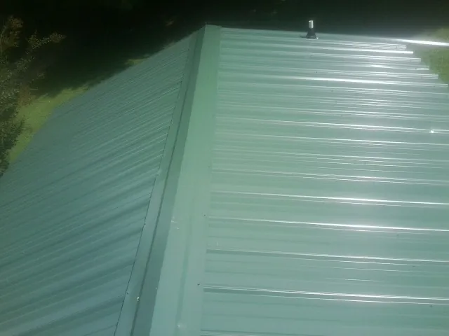 New green metal panels meeting at the ridge of a roof — Flat Roof Repair work by our crew in Swanville