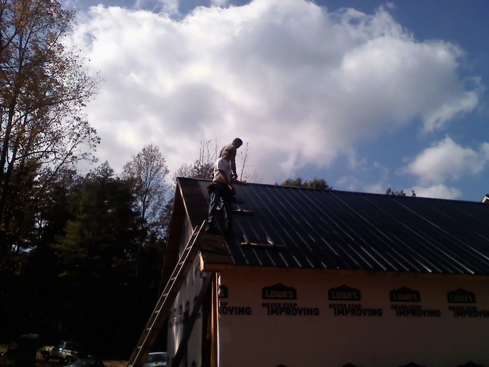 Roofer fastening dark metal panels high against a cloudy sky, from a Roof Inspection job in Swanville