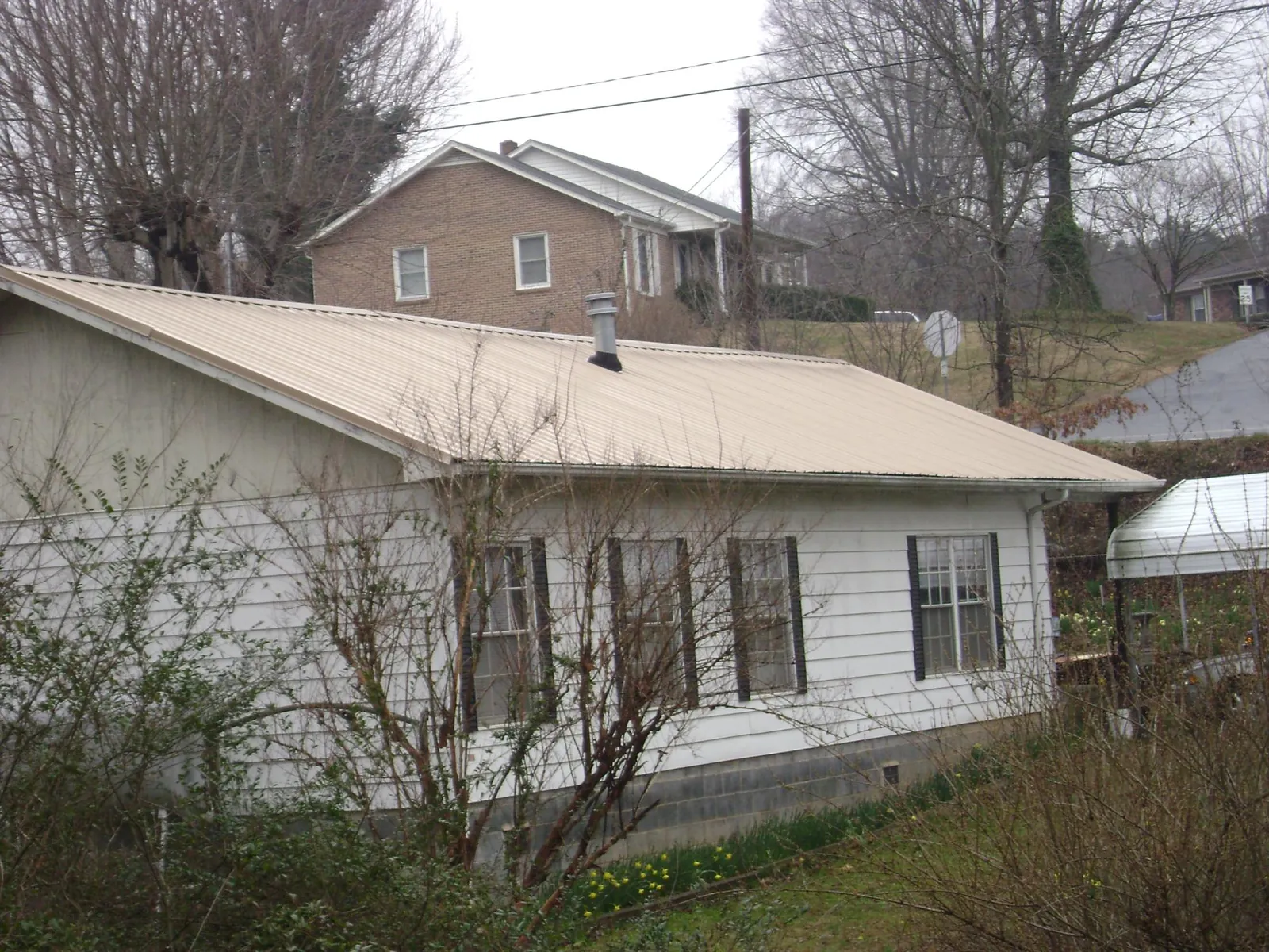Tan metal roof on a white sided house set into a hillside — Commercial Roofing by Roofing Brothers in Swanville