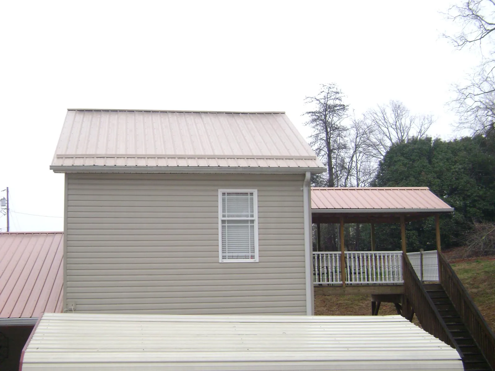 Tan metal roofs on a two story addition and attached porch, from a Roof Replacement job in Swanville